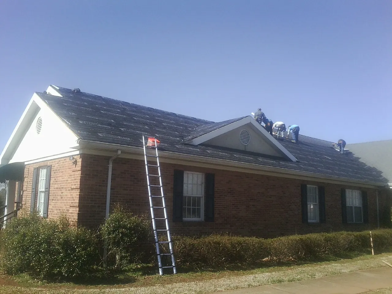 Crew tearing shingles off a brick ranch roof with a ladder set — Emergency Roof Repair work by our crew in Trufant