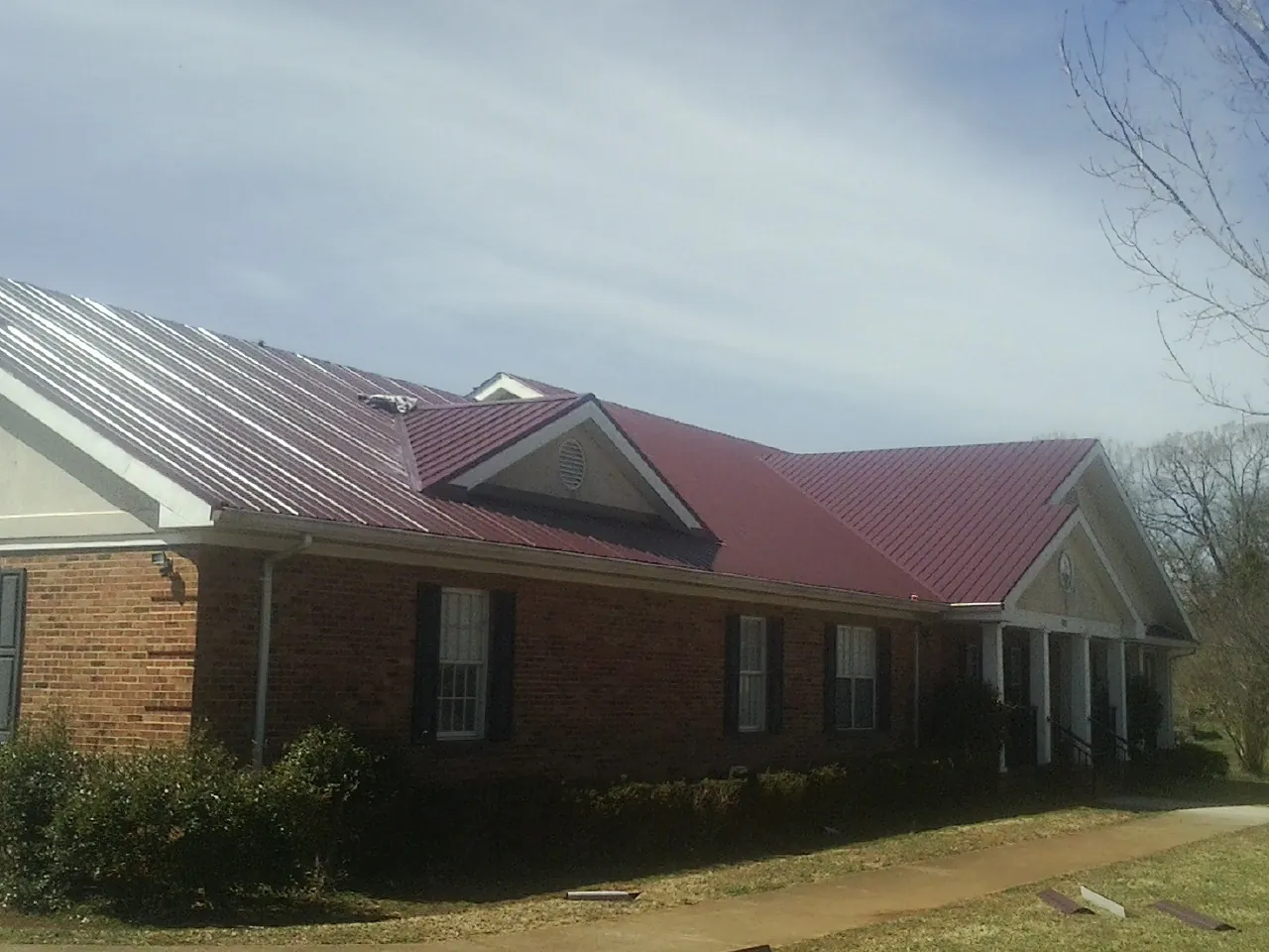 Red metal roof with gabled entries on a long brick building, from a Hail Damage Roof Repair job in Trufant