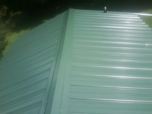 New green metal panels meeting at the ridge of a roof — Flat Roof Repair work by our crew in Trufant