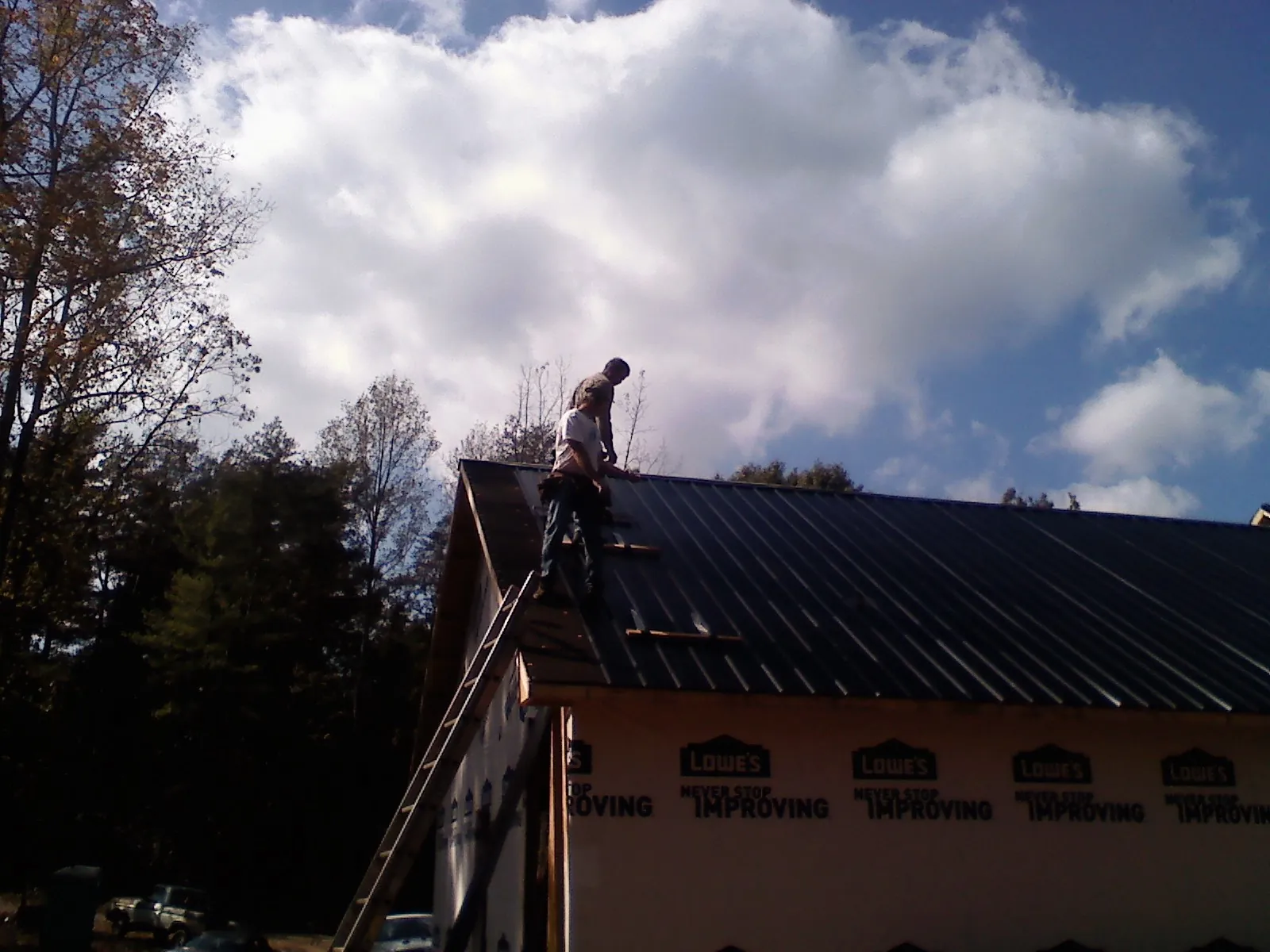 Roofer fastening dark metal panels high against a cloudy sky, from a Roof Inspection job in Trufant