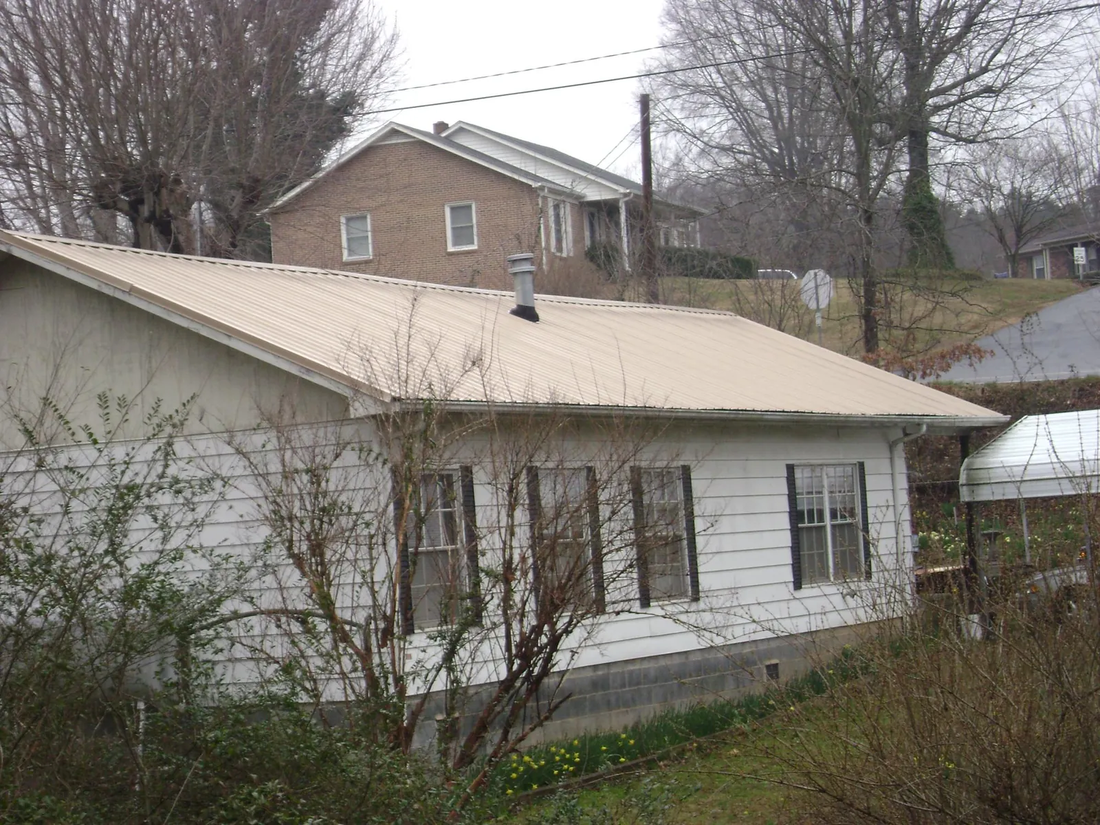 Tan metal roof on a white sided house set into a hillside — Commercial Roofing by Roofing Brothers in Trufant